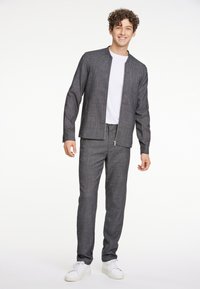 Grå rutigt jacka med matchande byxor, med dragkedja och en vit T-shirt under. Bärs med vita sneakers.