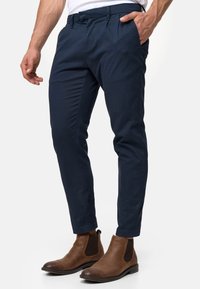Granatowe chinosy o wąskim kroju z wieloma kieszeniami, wykonane z lekkiego materiału. Połączone z brązowymi botkami Chelsea z elastycznymi bokami.