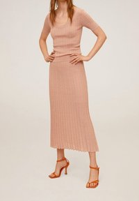 Vestido de punto acanalado rosa empolvado con mangas cortas y un cuerpo entallado, combinado con sandalias de tacón con tiras naranjas.