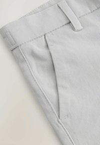 Pantaloni grigi chiari con frontale piatto, dettagli cuciti e tasche. Realizzati in tessuto liscio con una finitura pulita e sartoriale.