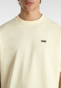 Hellgelbes Baumwoll-T-Shirt mit Rundhalsausschnitt und gesticktem schwarzen "VANS"-Logo auf der linken Brust. Weicher Stoff, lockerer Schnitt.