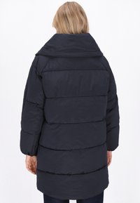 Jachetă puffer de marină cu guler înalt, buzunare laterale și un design matlasat. Materialul pare a fi neted și rezistent la apă.