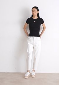 T-shirt nera aderente a maniche corte con logo ricamato, abbinata a jeans bianchi a vita alta con dettagli strappati e sneakers bianche.