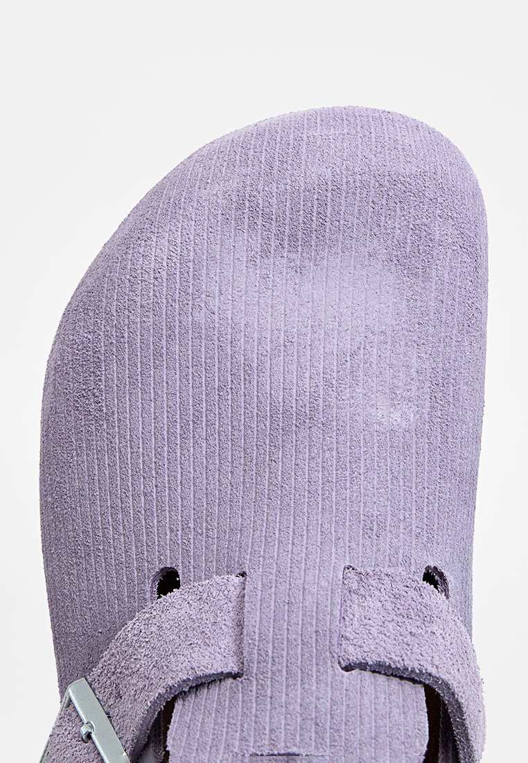 Nahaufnahme eines lila Wildlederclogs mit gerippter Textur und einem verstellbaren Riemen, der mit einer silbernen Schnalle versehen ist.