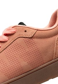 Rosa mockasinsneakers med texturerade prickar, svarta öglor och matchande snören. Har en låg profil och en stabil gummisula med subtila detaljer.
