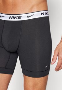 Boxers atléticos negros con una cinturilla elástica blanca que presenta el logo de Nike. Textura suave con un ajuste a medida y detalles de costura.