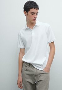 Bílá bavlněná polo košile s límečkem, krátkými rukávy a třemi knoflíky. Vybaveno s světle šedými džíny. Minimalistický design.