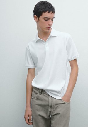 Weißes Baumwoll-Polohemd mit Kragen, kurzen Ärmeln und drei Knöpfen. Kombiniert mit hellgrauen Jeans aus Denim. Minimalistisches Design.
