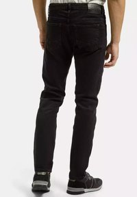 Czarne dżinsy w slim fit, z tylnymi kieszeniami i skórzaną naszywką na pasku. Nosi się je z czarnymi trampkami.