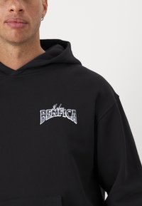 Black hoodie made of cotton with a front pocket. Features an embroidered logo "BENFICA" in silver lettering on the chest.