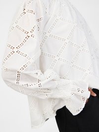 White blouse featuring intricate cut-out lace patterns, loose fit, gathered sleeve cuffs, and a soft, lightweight texture.