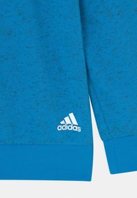 Felpa sportiva blu con texture a macchie, polsini a costine e orlo solido a contrasto. Logo Adidas in bianco.