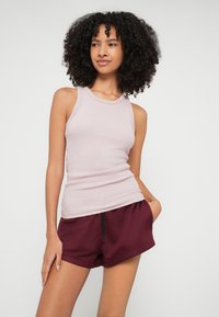 Ροζ ριμπ τοπ χωρίς μανίκια σε ανοιχτή απόχρωση, συνδυασμένο με σκούρα μπορντό σορτς. Το τοπ διαθέτει στρογγυλή λαιμόκοψη και εφαρμοστή γραμμή, ενώ τα σορτς έχουν ελαστική μέση.