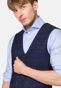 Granatowy tweedowy kamizelka o podwójnym zapięciu, z czerwono-białym wzorem w kratę, dopełniona jasnoniebieską koszulą z guzikiem.