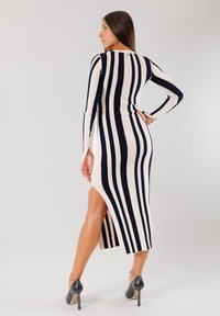 Abito in maglia con strisce verticali blu navy e crema, maniche lunghe, spacchi laterali, texture a costine e scarpe con tacco alto.