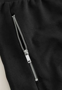 Lähivõte osaliselt avatud hõbedasest metallist tõmblukust musta riide peal, kus on nähtavad õmblused ja tekstuur.