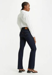 Donkerblauwe denim flared jeans met contrasterende gouden stiksel en details op de achterzak. Gekocht met een losse, witte overhemd met knopen.