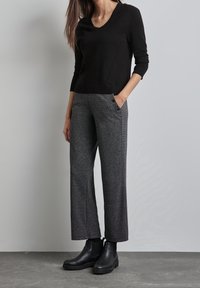 Black v-neck knit sweater paired with gray textured wide-leg pants, featuring side pockets and black ankle boots. Flat surface background.