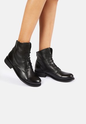 Stivali alla caviglia in pelle nera con design con lacci, tacco basso e superficie texture, dotati di una cerniera laterale per una facile calzata.