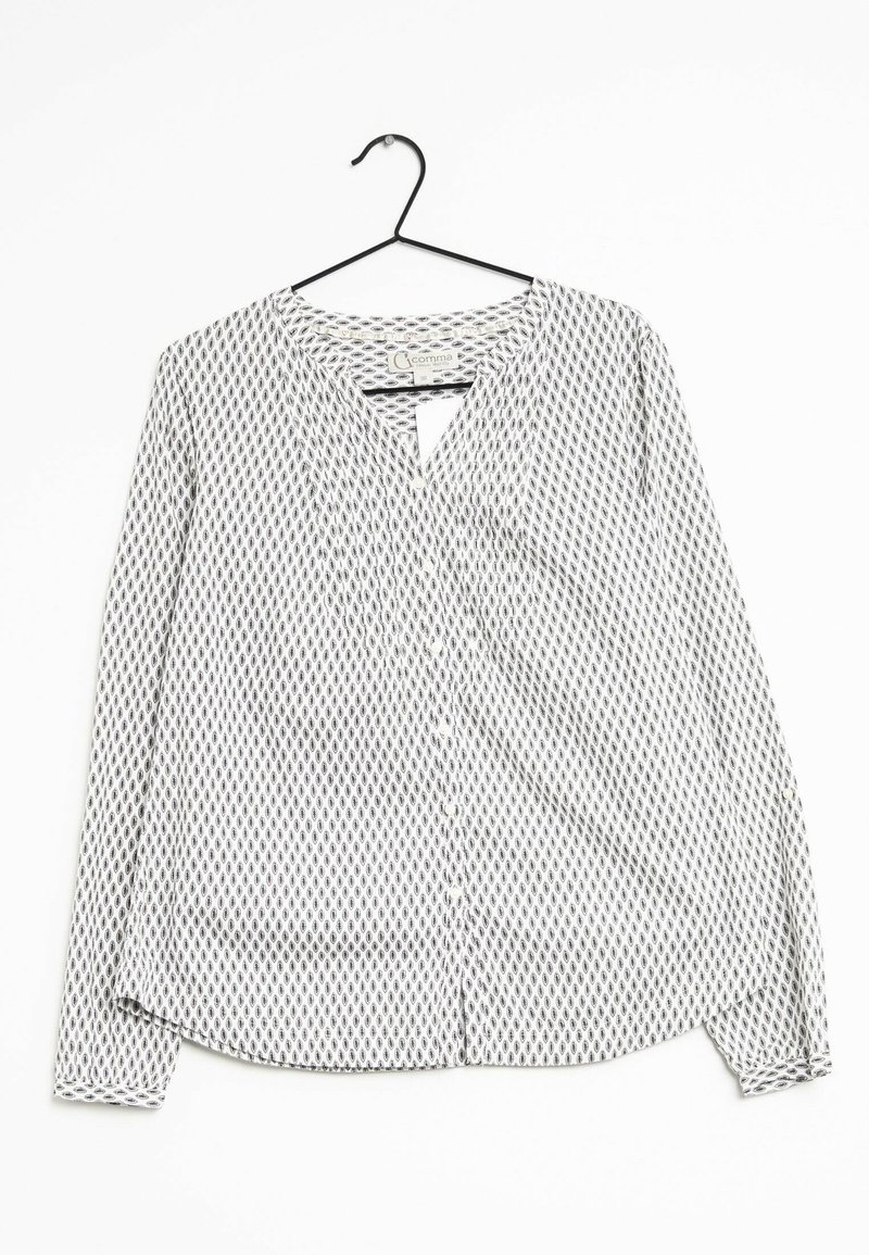 Blouse blanche à manches longues avec un petit motif losange noir, boutonnée sur le devant et col rond, suspendue sur un cintre noir sur fond blanc.