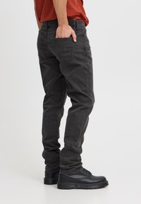 Mustad teksapüksid sirge lõikega, millel on tagataskud ja tekstuurse viimistlusega, kantud mustade paeltega saapadega.