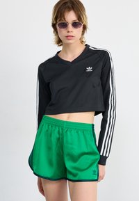 Black cropped long-sleeve shirt with a V-neck and white stripes, paired with green satin shorts featuring an elastic waistband and logo.