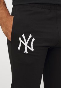 Melnas sporta bikses ar mīkstu tekstūru, kas rotātas ar lielu baltu New York Yankees logotipu kreisajā augšstilbā un elastīgu jostasvietu.