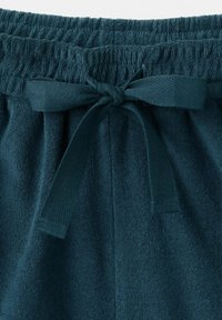 Ceinture élastique avec un nœud de cordon en tissu noué sur un pantalon ou un short texturé bleu sarcelle foncé.