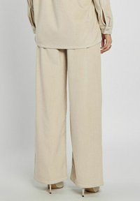 Beżowe spodnie dzwony z korduroju charakteryzują się miękką teksturą, luźnym krojem i delikatnym rozszerzeniem u dołu. Idealne do casualowych stylizacji lub warstwowego ubioru.