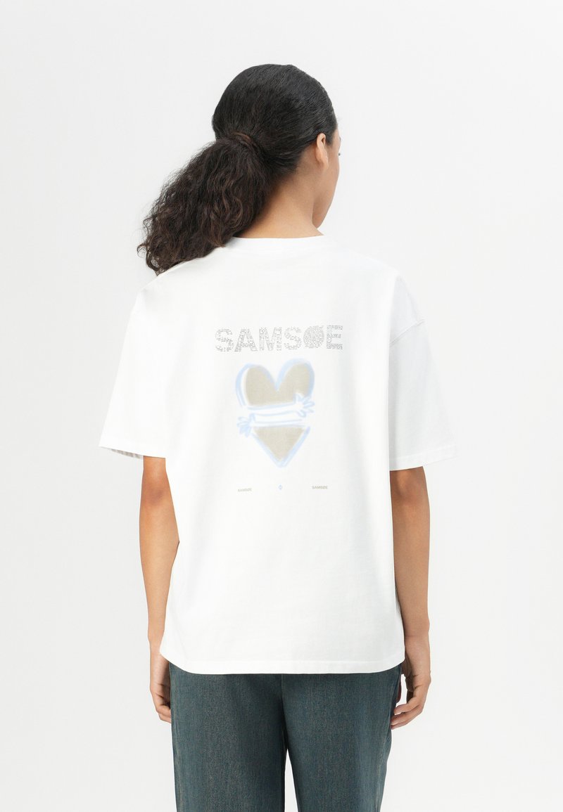 White cotton T-shirt with short sleeves, featuring "SAMSOE" text and a heart graphic in blue and beige on the back. Relaxed fit design.