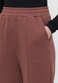 Rožinės spalvos jogger'iai su elastinga juosmena, šoninėmis kišenėmis ir minkšta tekstūra. Dizainas pasižymi švariais linijomis ir laisvu pritaikymu.