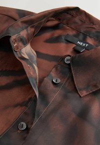 Rudas ir juodas raštuotas marškinis su mygtukų uždarymu, apykakle ir audinio etiketė, pažymėta "NEXT". Lygus tekstūra ir lengvas dizainas.