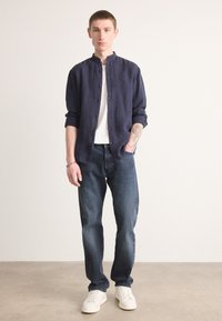 Marine linnen skjorte med stående krave, hvit crew neck t-skjorte, mørkeblå jeans og hvite joggesko. Slim fit, casual stil.