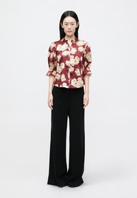 Μπορντό μπλούζα με λουλούδια και κοντά φουσκωτά μανίκια, με κουμπιά μπροστά, συνδυασμένη με μαύρο παντελόνι φαρδιάς γραμμής. Λείο ύφασμα, έντονο λουλουδάτο σχέδιο.