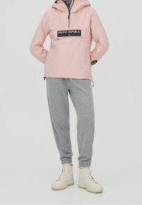 Lys pink pullover jakke med et sort "PACIFIC REPUBLIC" logo, parret med grå sweatpants og creme ankelstøvler.