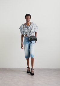 Top texturizado de mangas bufantes multicoloridas, calções de bermuda em denim azul-claro com bainha desfiada, mala preta e sandálias pretas de salto.