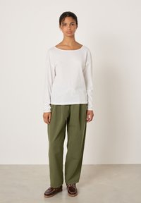 Valge puuvillane pika varrukaga pluus, mida kannab oliivroheliste volditud pükstega ja pruunide pitsiga jalanõudega, omades lõdvestunud lõiget ja minimalistlikku disaini.