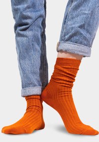 Pomarańczowe skarpetki z prążkami o dopasowanym kroju, zestawione z podwiniętymi jasnoniebieskimi dżinsami, ukazujące miękką fakturę i żywy kontrast kolorów.