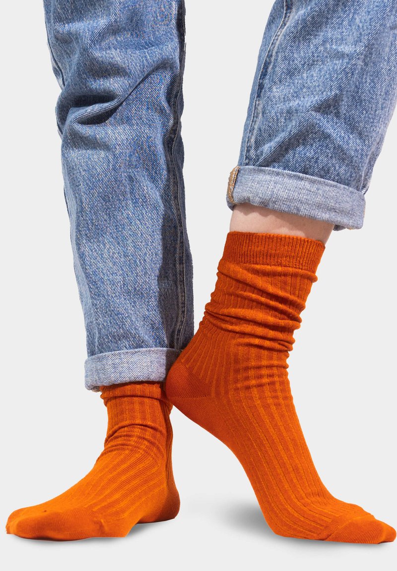 Pomarańczowe skarpetki z prążkami o dopasowanym kroju, zestawione z podwiniętymi jasnoniebieskimi dżinsami, ukazujące miękką fakturę i żywy kontrast kolorów.