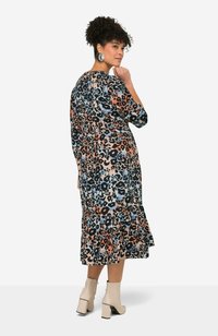 Robe imprimée léopard dans des teintes d'orange, de bleu et de noir ; présente un corsage ajusté, des manches trois-quarts et un ourlet volanté. Portée avec des bottines beiges.