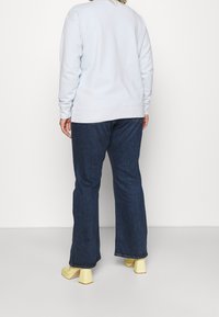 Lysblå sweatshirt med rund halsudskæring og ribbede manchetter, parret med mørke denim flare jeans og gule blokhælede sko.