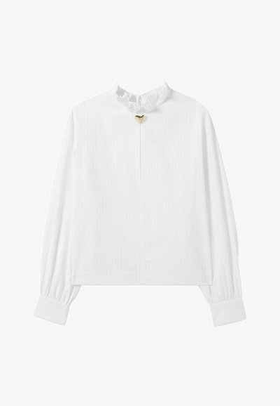 Blouse blanche à manches longues avec un col à volants et un petit détail en forme de cœur doré au centre, arborant des rayures verticales sur l'ensemble.