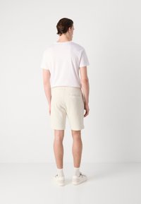 Maglietta bianca a maniche corte abbinata a pantaloni corti cremosi con texture, dotati di una sola tasca sul retro, indossati con sneaker bianche e calzini grigio chiaro.