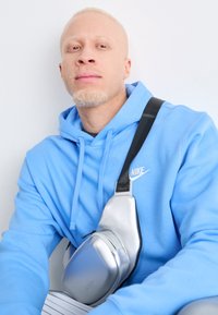 Sweatshirt com capuz da Nike em azul claro, acompanhado por uma elegante bolsa a tiracolo prateada com fecho de zip e alça preta.