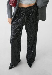 Sorte palazzo-bukser med palietter og snoreliv, sat sammen med en grå cropped sweater og skarpe sorte spidse hæle.