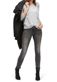 Šedý svetr s řasenými rukávy, kombinovaný s tmavě šedými skinny džíny a černými kotníkovými botami. Černý kabát je přehozený přes rameno.
