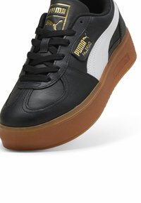 Fekete-fehér bőrsneaker fényes felülettel, vastag gumitalppal és arany logós részletekkel a nyelvnél.