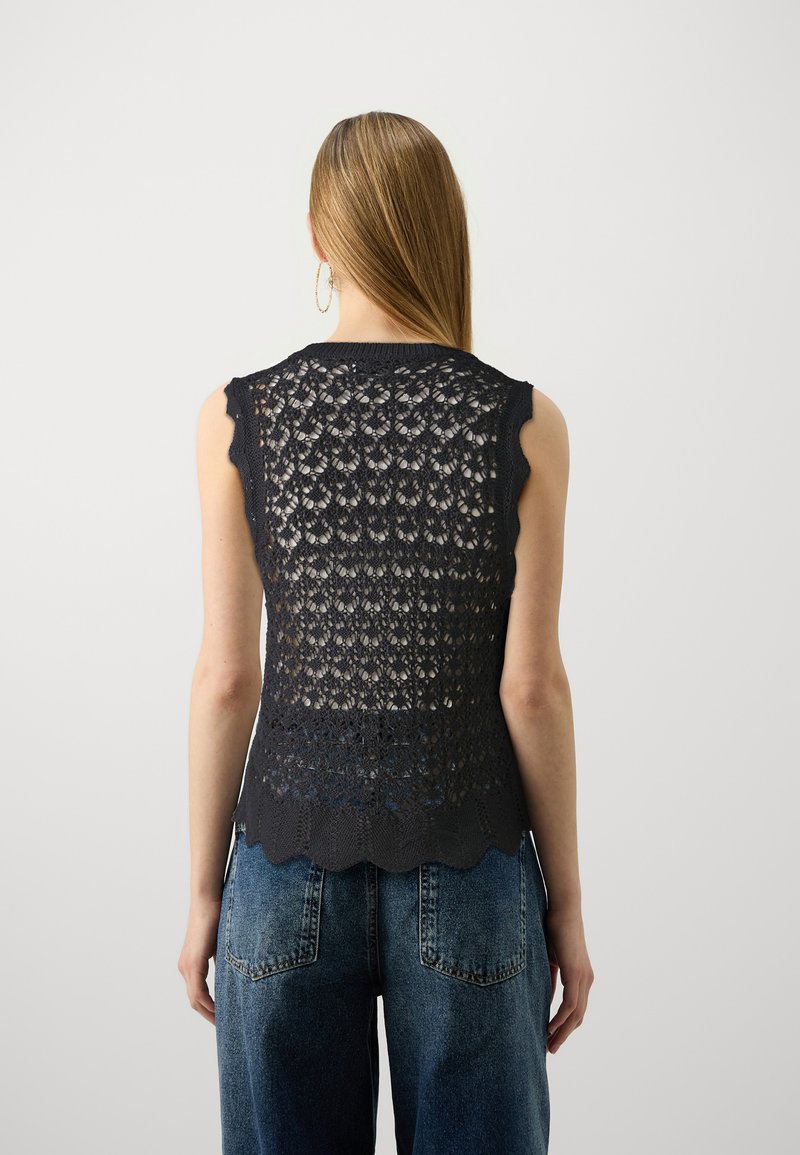 Dunkelblaues gestricktes ärmelloses Oberteil mit gezackten Kanten und aufwendigem Spitzenmuster; kombiniert mit hochtaillierten Jeans.