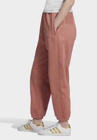 Rosa svettbyxor med elastiskt midjeband, sidofickor och broderad logotyp. Matchas med vita sneakers med guldaccent.