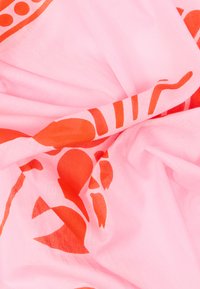 Ροζ ύφασμα με κόκκινα αφηρημένα σχήματα και σχέδια, σφιχτά ζαρωμένο και διπλωμένο στο κέντρο.